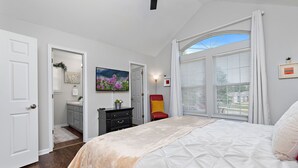 A bedroom with a large bed, a red chair, a painting, and a view through the window.