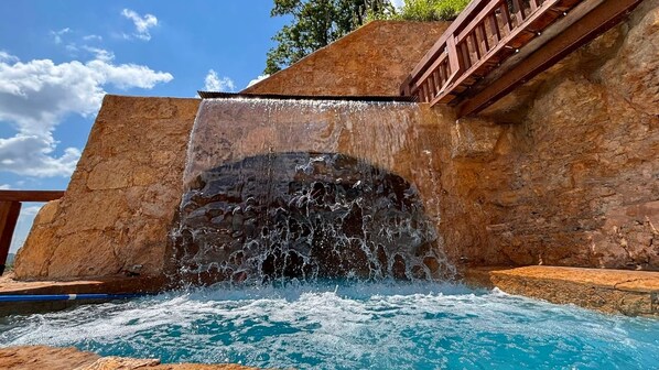 Una piscina con cascada, rodeada de muros de piedra y una terraza de madera.