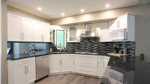 Una cocina moderna con armarios blancos, encimera negra y salpicadero de piedra.