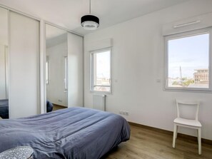 A modern bedroom with a bed, a chair, and a large window offering a city view.