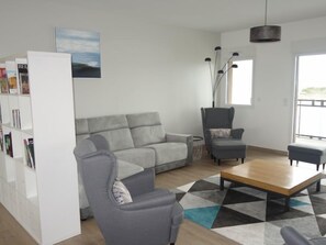 A modern living room with a grey sofa, a grey armchair, a wooden coffee table, and a bookshelf.