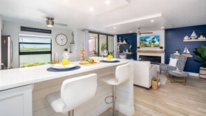 A modern kitchen with a large island, bar stools, a dining area with a patterned sofa, and a fireplace.