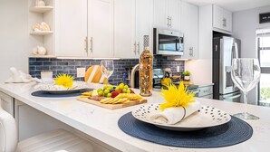 A modern kitchen with white cabinets, a marble countertop, and a variety of fruits and a bottle of liquor.