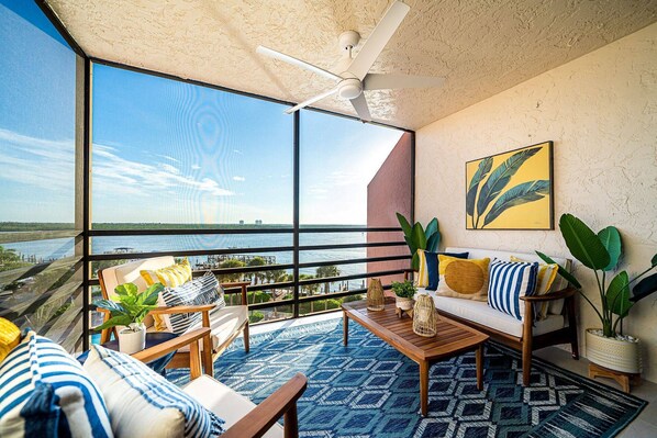 A spacious balcony with a view of the water, furnished with a sofa, chairs, and a coffee table.