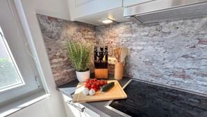 Una cocina con salpicadero de pared de piedra, una planta en maceta, tabla de cortar con verduras y una estufa.