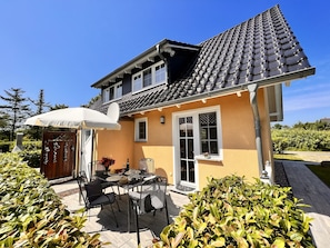 Ein zweistöckiges Haus mit Ziegeldach, einer Terrasse mit Tisch und Stühlen und einem Garten.