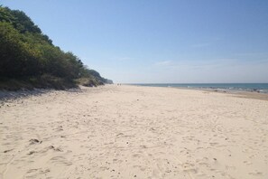 Ein weiter Sandstrand mit Fußspuren, einem klaren Himmel und einem Blick auf das Meer in der Ferne.