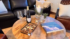 Una mesa redonda de madera con una botella de vino rosado, copas, una vela y un libro.