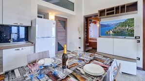 Una cocina moderna con comedor, refrigerador, televisor y vistas panorámicas a un lago y montañas.