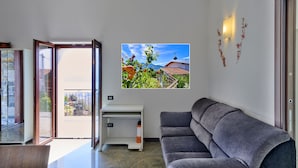 Un salón moderno con un sofá gris, un escritorio blanco y un amplio ventanal con vistas a un jardín y montañas.