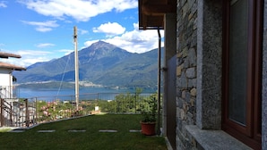 Un balcón con un muro de piedra, vistas a un lago, montañas y cielo despejado.
