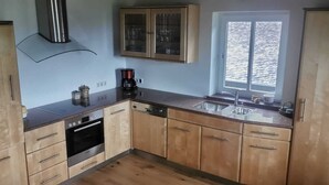 A compact kitchen with wooden cabinets, a built-in oven, a coffee maker, and a window with blinds. - VACATION AT THE FARM HIDEAWAY IN THE ALPS (Stuhlfelden)