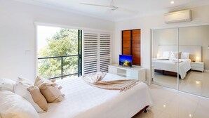 A modern bedroom with a large bed, a TV, and a balcony with white shutters. - Anchorage 14, Anchorage 14 on Hamilton Island (Hamilton Island)
