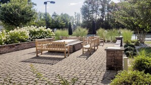 An outdoor patio with wooden benches and tables, surrounded by brick walls and greenery. - Gorgeous 3 BR, 2.5 BA, 5 Miles to Bethany Beach, Pool, Tennis, Walking Trails, and Free Activities! (Frankford)
