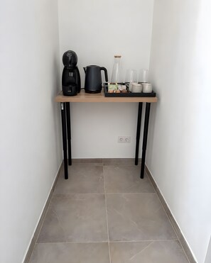 Un coin cuisine avec une machine à café, une bouilloire et de la verrerie, le tout posé sur une table en bois.