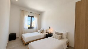 Un dormitorio con dos camas, una mesita de noche con lámpara y una ventana con cortinas.