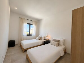 Una camera da letto con due letti, un comodino con una lampada e una finestra con tende.
