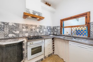 Una cucina con piastrelle decorate, un fornello a gas, un forno integrato e una finestra con cornice in legno.