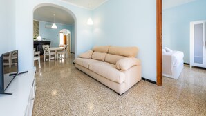 Una sala de estar moderna con un sofá color crema, un comedor con mesa y sillas, y una cocina visible a través de un arco.