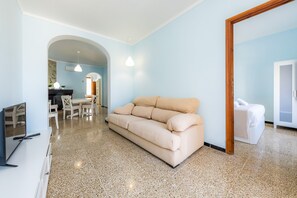 Un soggiorno moderno con un divano beige, un'area pranzo con tavolo e sedie, e una cucina visibile attraverso un arco.