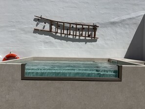 Une piscine rectangulaire à l’eau claire, une structure en bois fixée au mur et une bouée rouge.