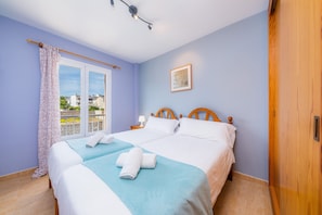Een tweepersoonsbed met witte lakens, een blauwe decoratieve plaid en twee handdoeken op het bed.