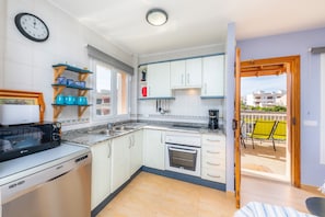 Een keuken met witte kastjes, een magnetron, een vaatwasser en uitzicht op een terras.