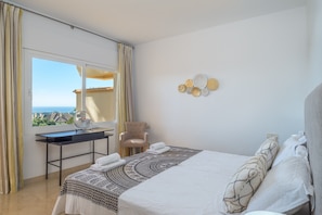A bedroom with a bed, a desk, a chair, a window with curtains, and decorative wall art.