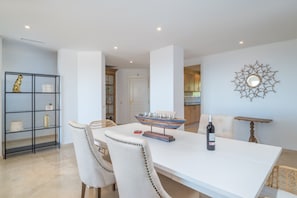 A dining area with a white table, two chairs, a decorative centerpiece, and a bottle of wine.