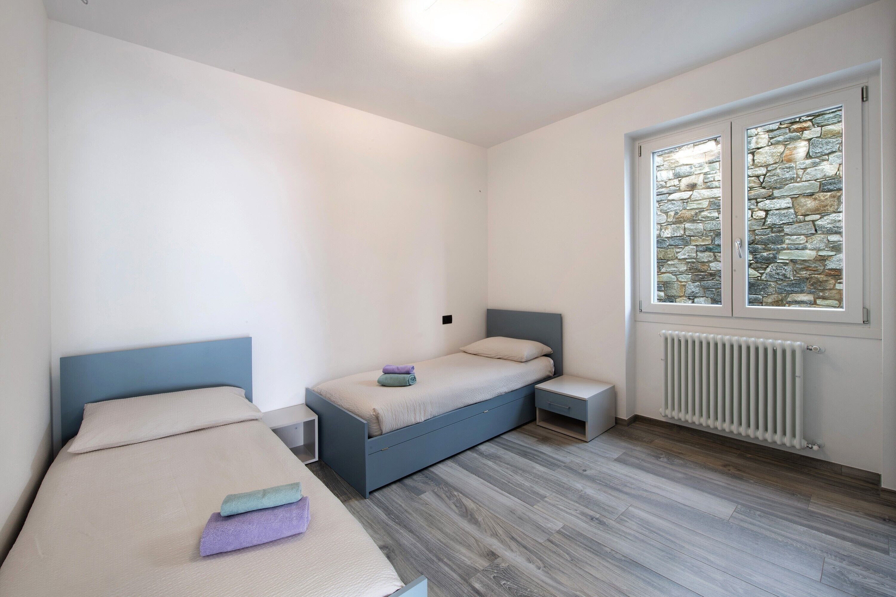 Un dormitorio con dos camas, una ventana y una pared de piedra, además de un radiador.