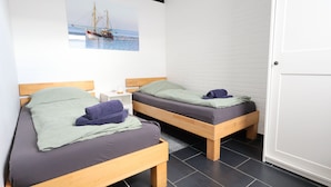 Zwei hölzerne Betten mit grau- und grün gestreuter Bettwäsche, ein weißer Nachttisch und ein an der Wand hängendes Bild von einem Boot auf dem Meer.