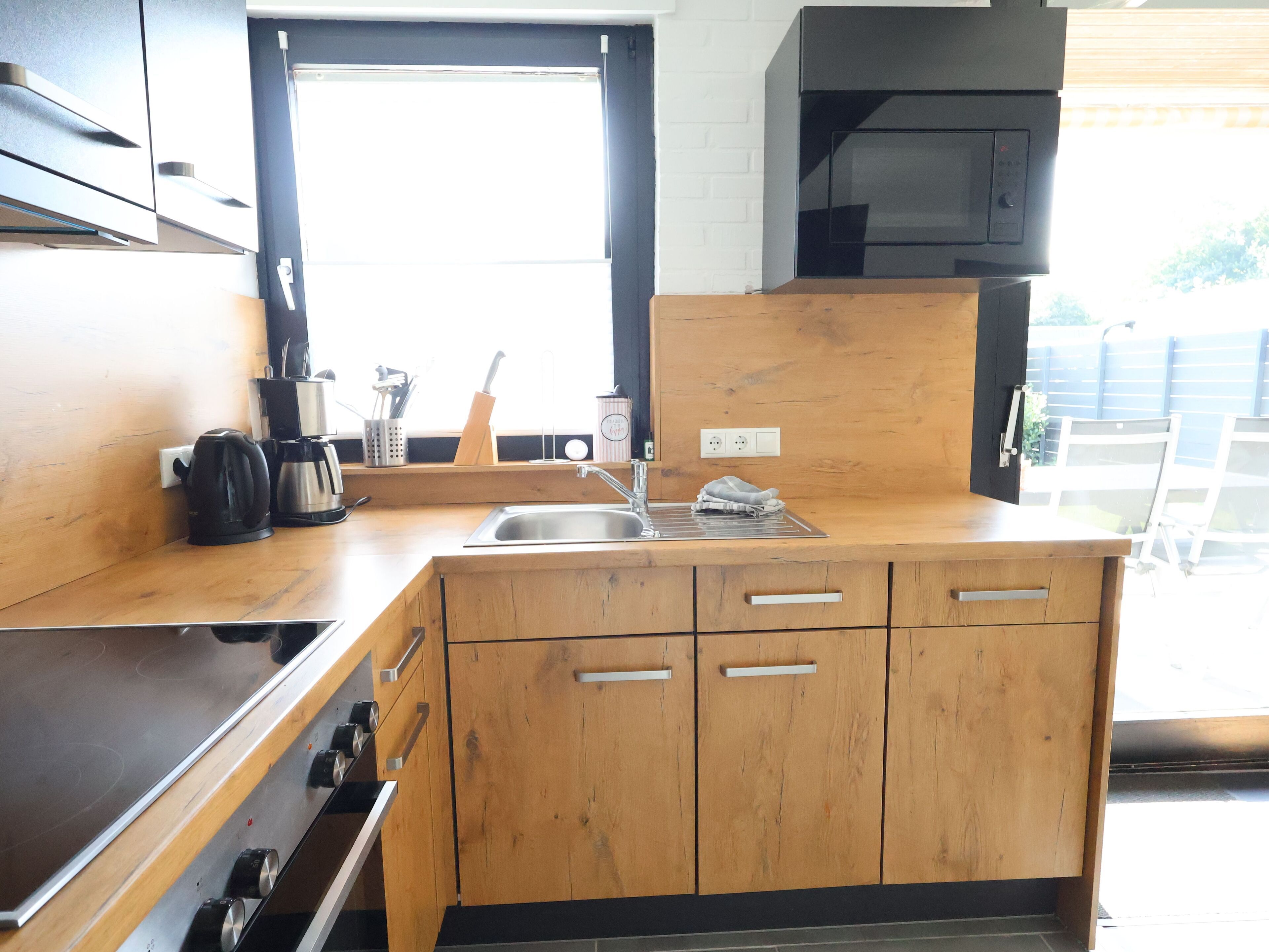 A modern kitchen with wooden cabinets, a stainless steel sink, and a black microwave.