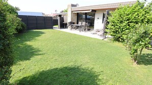 Ein Garten mit einer Terrassenfläche, einem Grill und einem überdachten Sitzbereich.