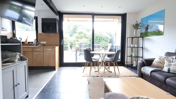 Eine moderne Küche mit Essbereich, einer Couch und Blick durch eine Glastür.