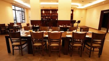 A dining area with multiple tables and chairs, a large window, and a bookshelf in the background.