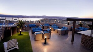 A rooftop terrace with wicker furniture and blue cushions, overlooking a cityscape and water. - BAITY Boutique Hotel (Aqaba)
