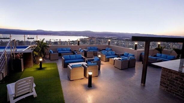 Terraza en la azotea con mobiliario de mimbre y cojines azules, con vistas a un paisaje urbano y al agua.