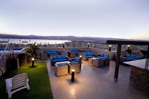 A rooftop terrace with wicker furniture and blue cushions, overlooking a cityscape and water. - BAITY Boutique Hotel (Aqaba)