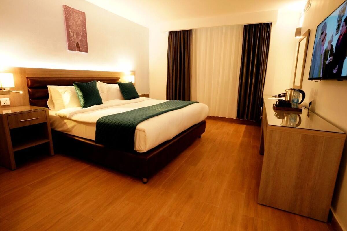 A hotel room with a bed, bedside table, lamp, TV, and curtains.