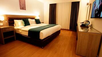 Habitación de hotel con cama, mesita de noche, lámpara, televisión y cortinas.