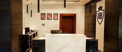 A reception area with a marble reception desk, black pendant lights, framed pictures on the wall, and a wooden door.
