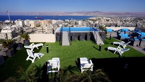 Terraza en la azotea con piscina, sillas de descanso y vistas a la ciudad y al mar.