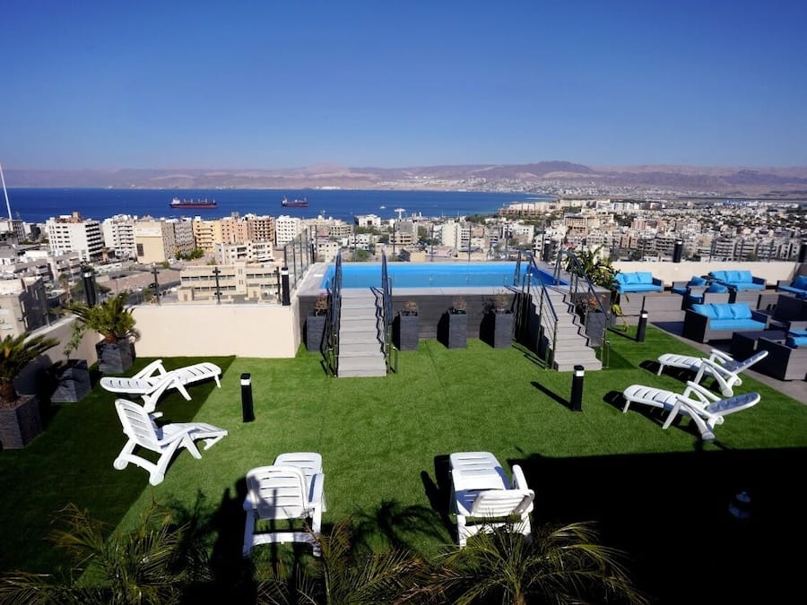 Terraza en la azotea con piscina, sillas de descanso y vistas a la ciudad y al mar.