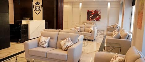 A modern hotel lobby with a reception desk, sofas, and a glass coffee table.