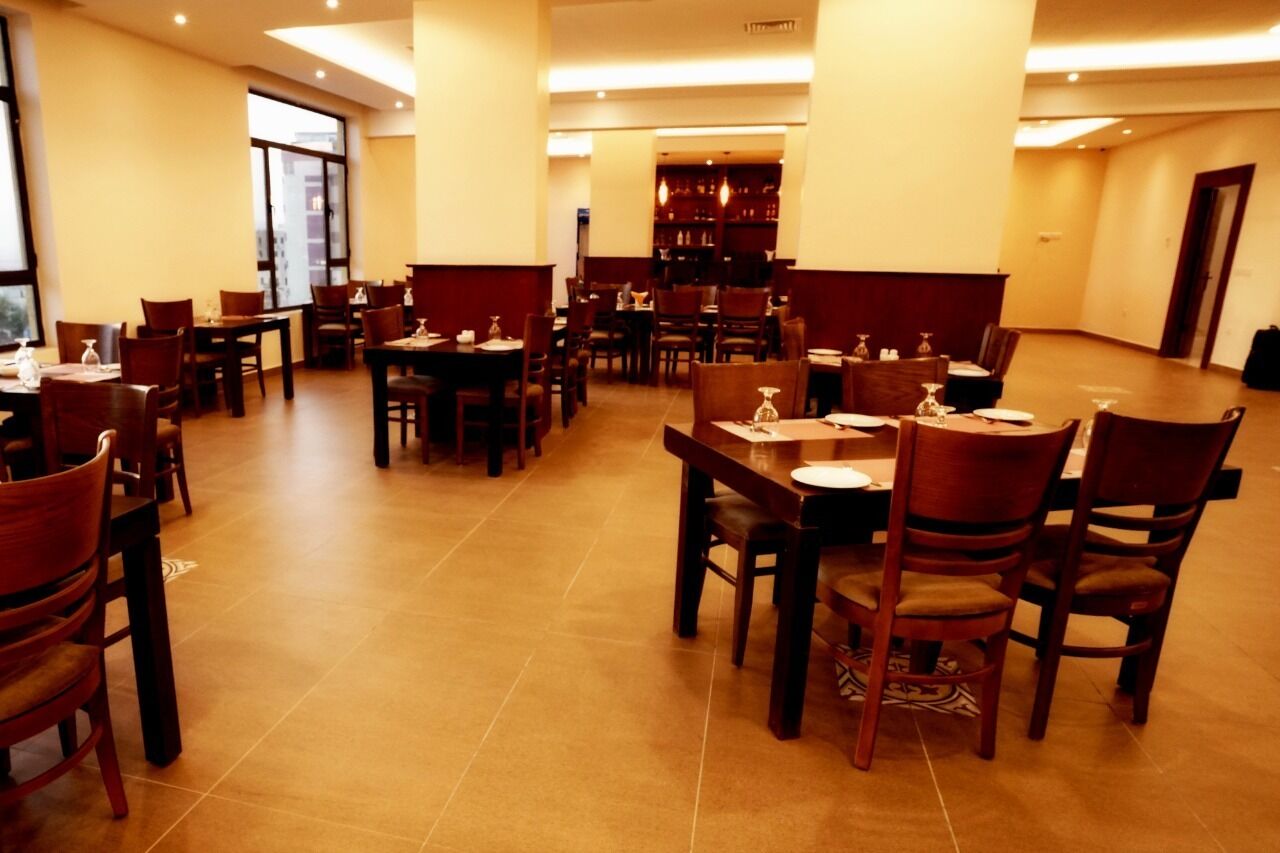 Amplio comedor de hotel con varias mesas y sillas, una barra central y grandes ventanales que permiten la entrada de luz natural.
