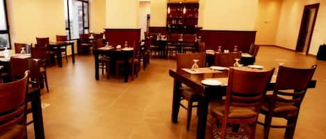 Amplio comedor de hotel con varias mesas y sillas, una barra central y grandes ventanales que permiten la entrada de luz natural.