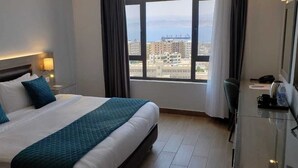 Habitación de hotel con una cama grande, un escritorio con una silla, un televisor y vistas a la ciudad por la ventana.