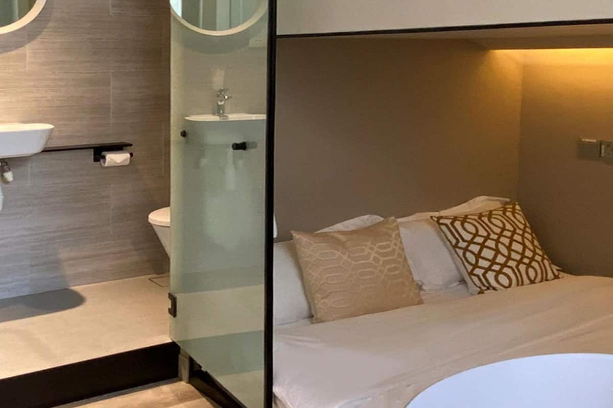 A compact hotel room with a bed, a bedside table, a mirror, and a bathroom with a toilet and sink.