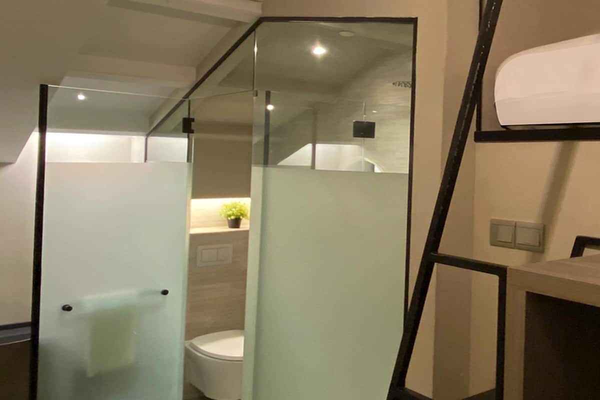 A compact bathroom with a glass partition, a toilet, and a small shelf with a plant.