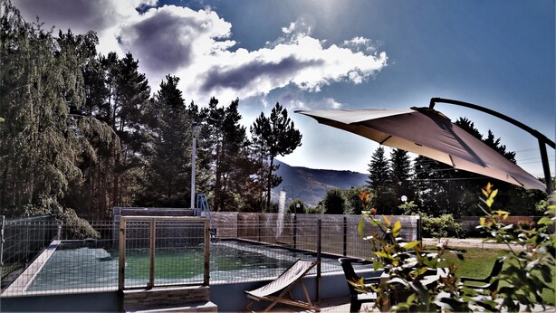 A swimming pool with a wooden deck, surrounded by a metal fence, and a large umbrella providing shade. - Vila Ambasador Bratin Dol (Bratin Dol)